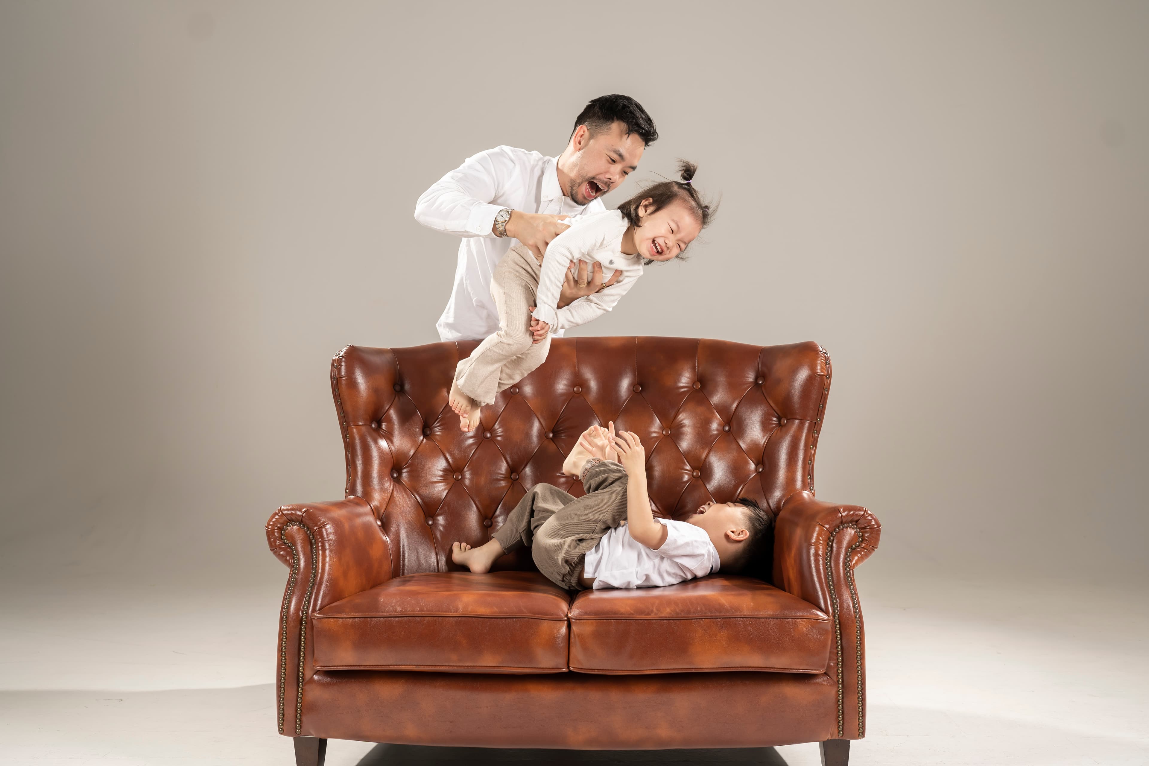 Cultiv8 founder playing with two young children on a leather sofa in a bright studio setting.